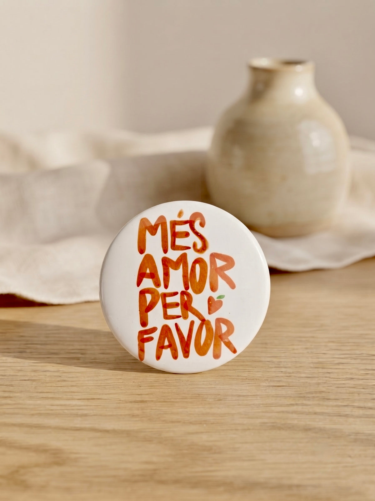Chapa Més Amor Per Favor Terreta – vista en entorno natural sobre madera