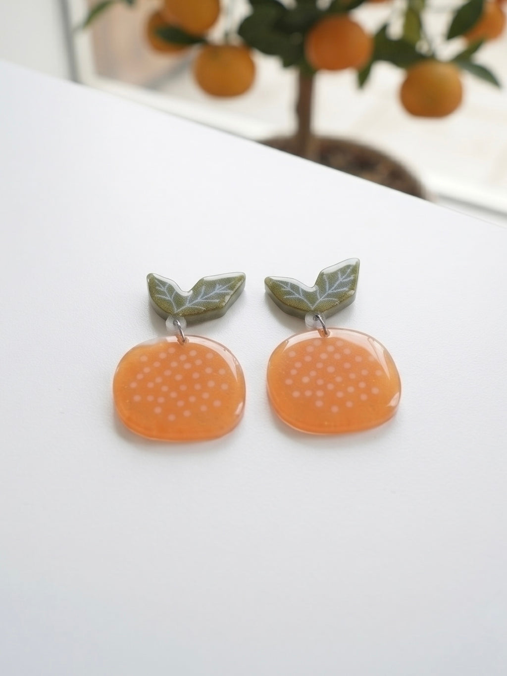 Pendientes mandarina Terreta sobre superficie blanca con naranjo de fondo