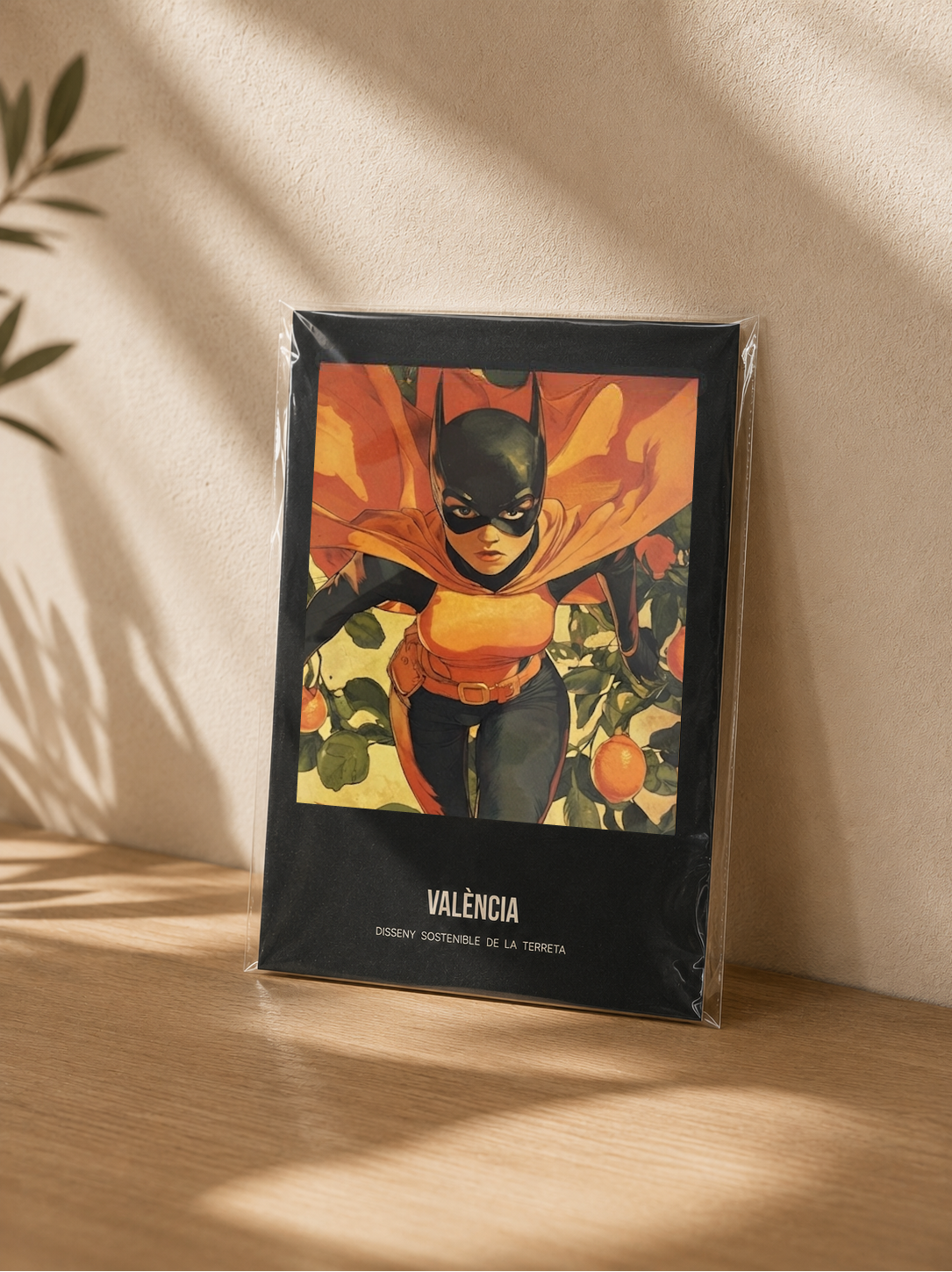 Poster València Superheróina – Mockup lámina A5 en funda transparente apoyada en madera, ilustración cómic valenciana Terreta